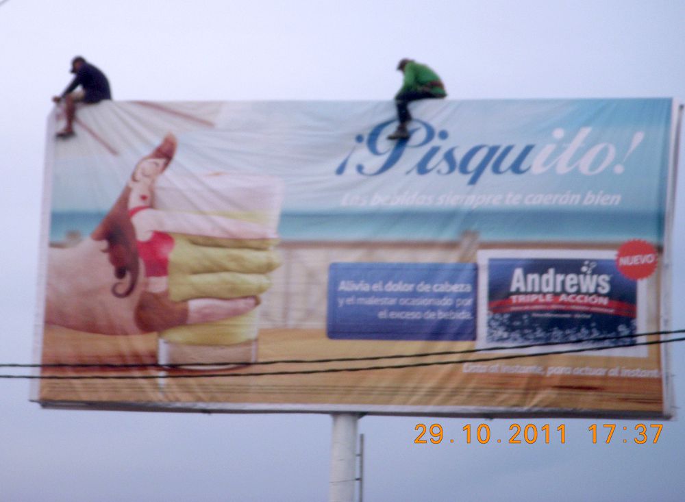 Hombres ubican paneles publicitarios sin seguridad.